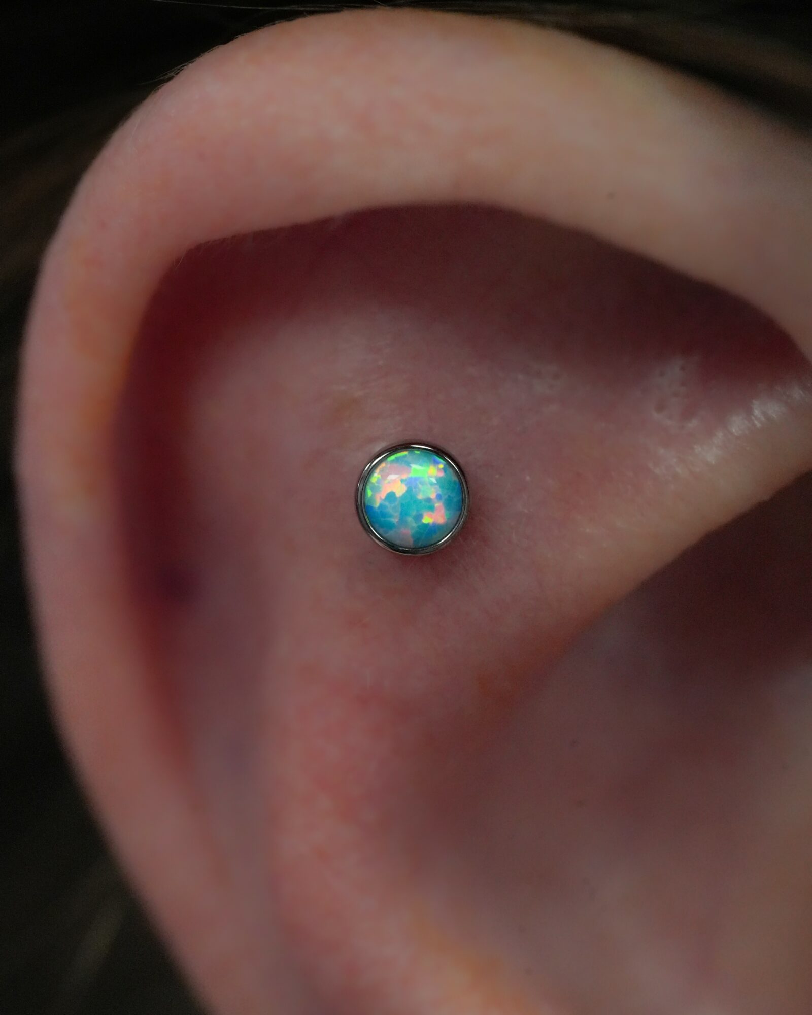 Close-up of a pierced ear with a small, round, colorful gemstone stud earring inside the ear canal.