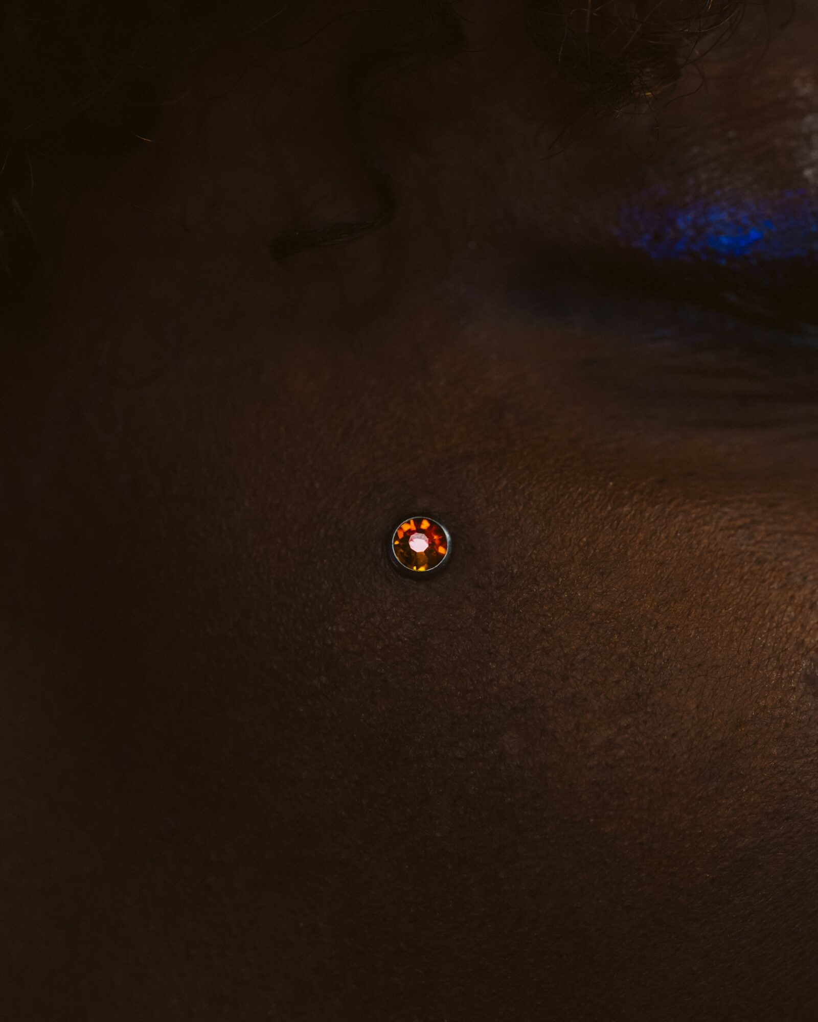 Close-up of a person's skin with a small, round, shiny object in the center, possibly a piercing or jewelry.