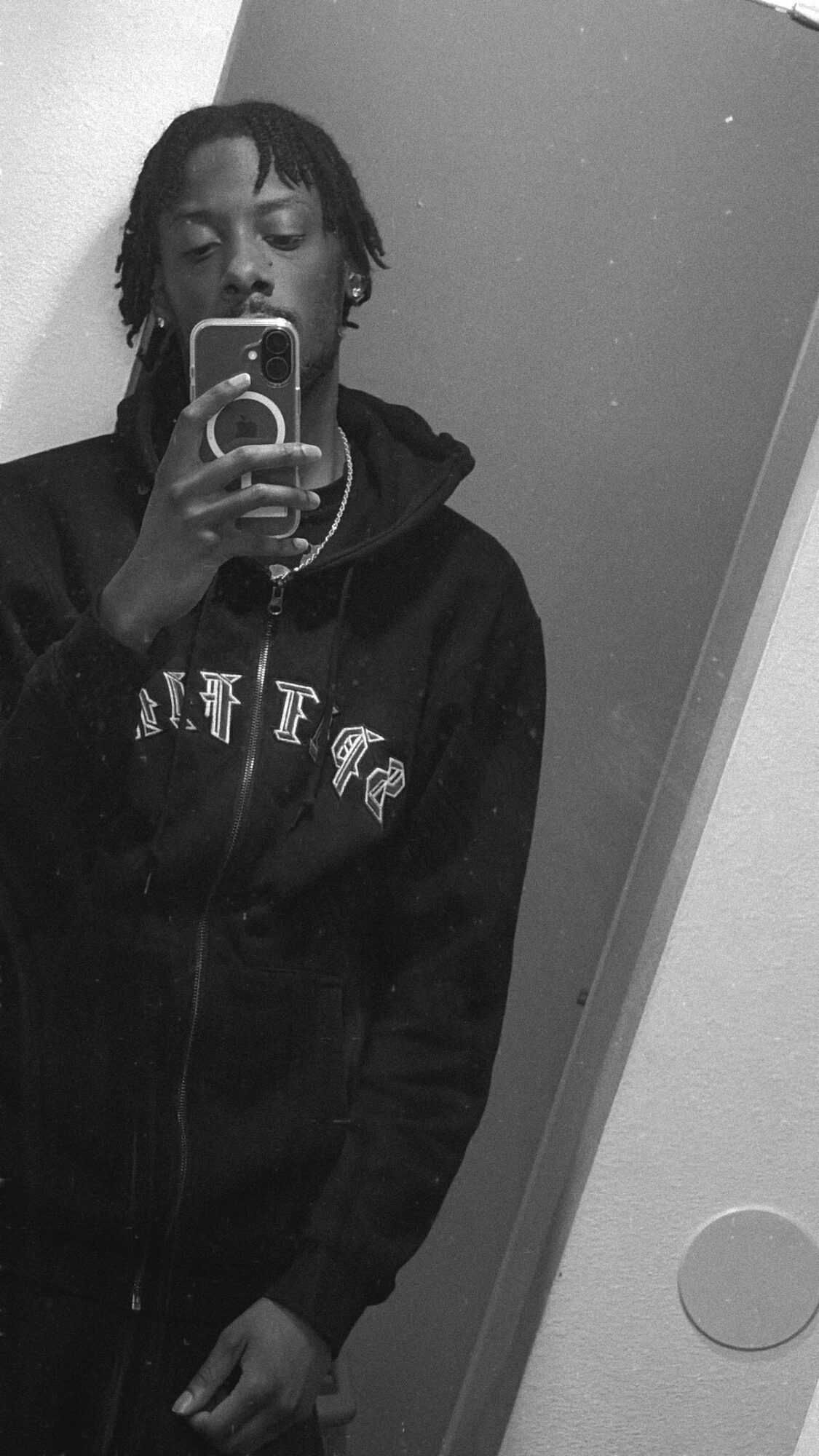 Person taking a mirror selfie with a phone, wearing a hoodie, in black and white.