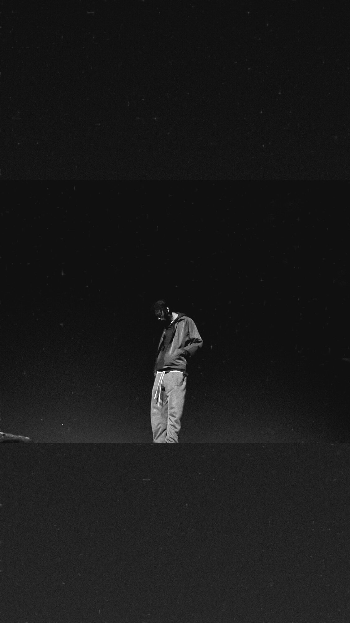 Person standing outdoors at night, looking down, with a starry sky above, in black and white.
