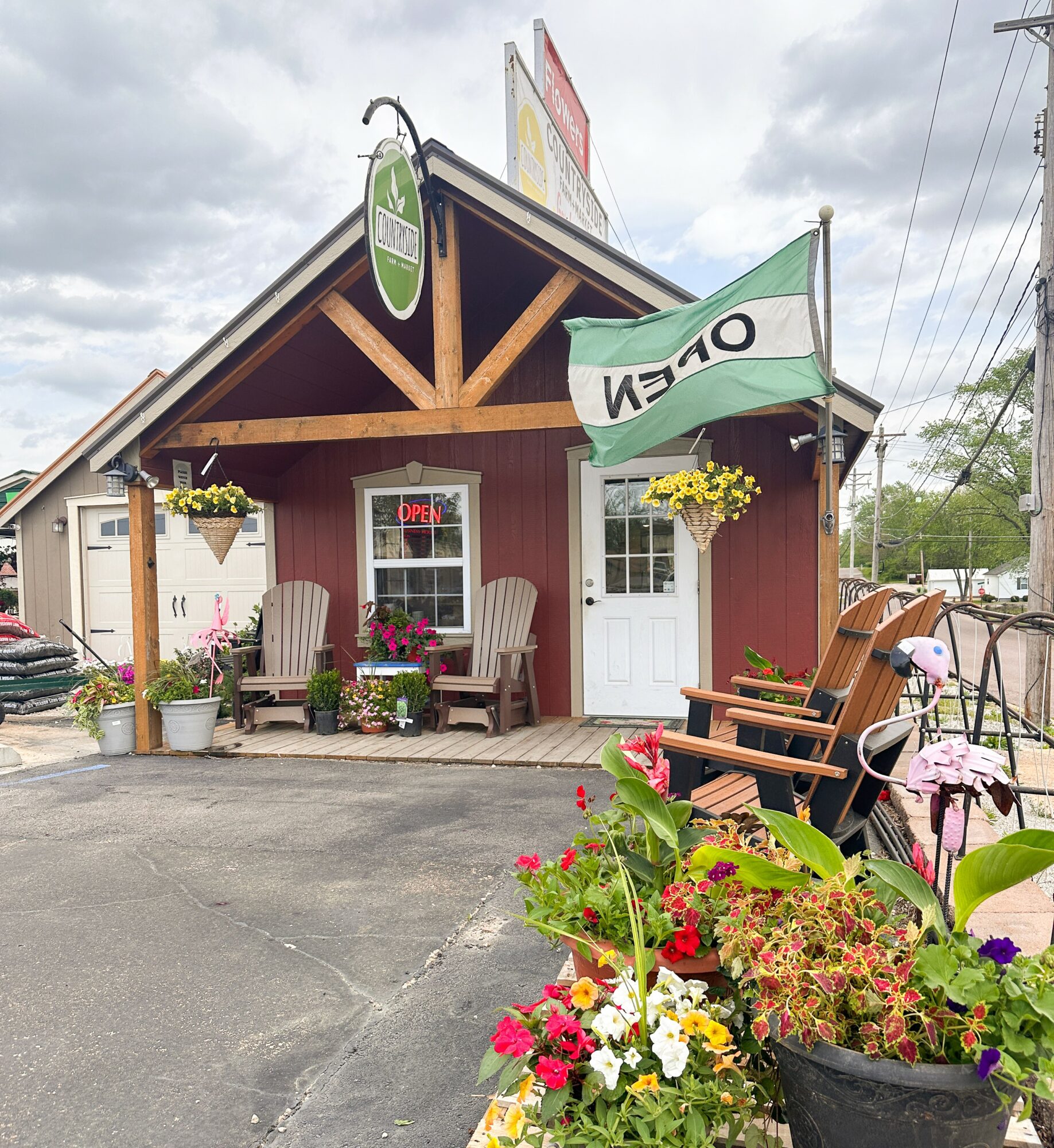 Small building with a porch, hanging flower baskets, chairs, and an open sign, under a cloudy sky.