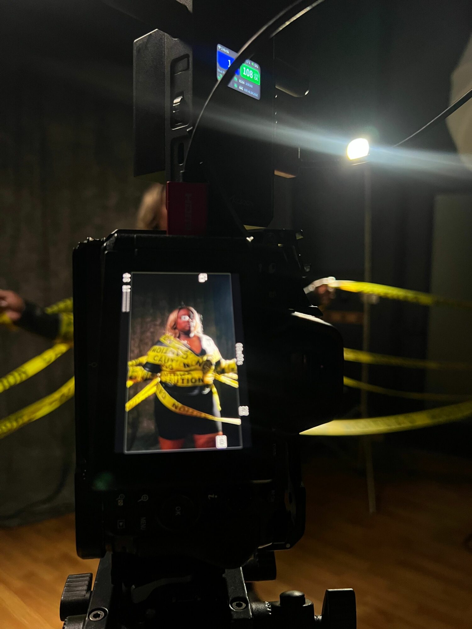 Camera view of a person holding yellow measuring tape, with a wooden floor in the background.