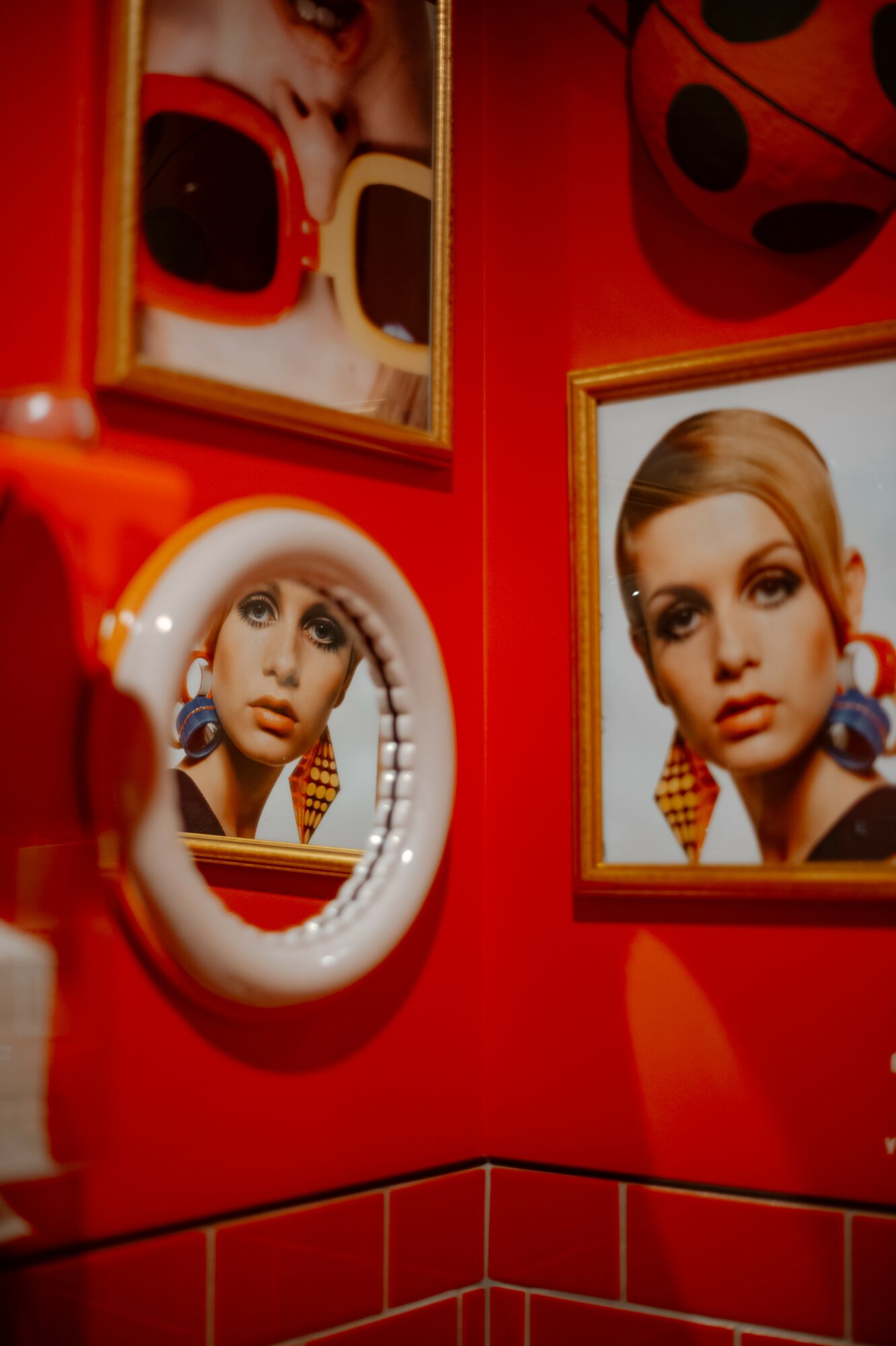 Red wall with framed photographs of a woman, a mirror, and a large ladybug decoration, all in a colorful setting.