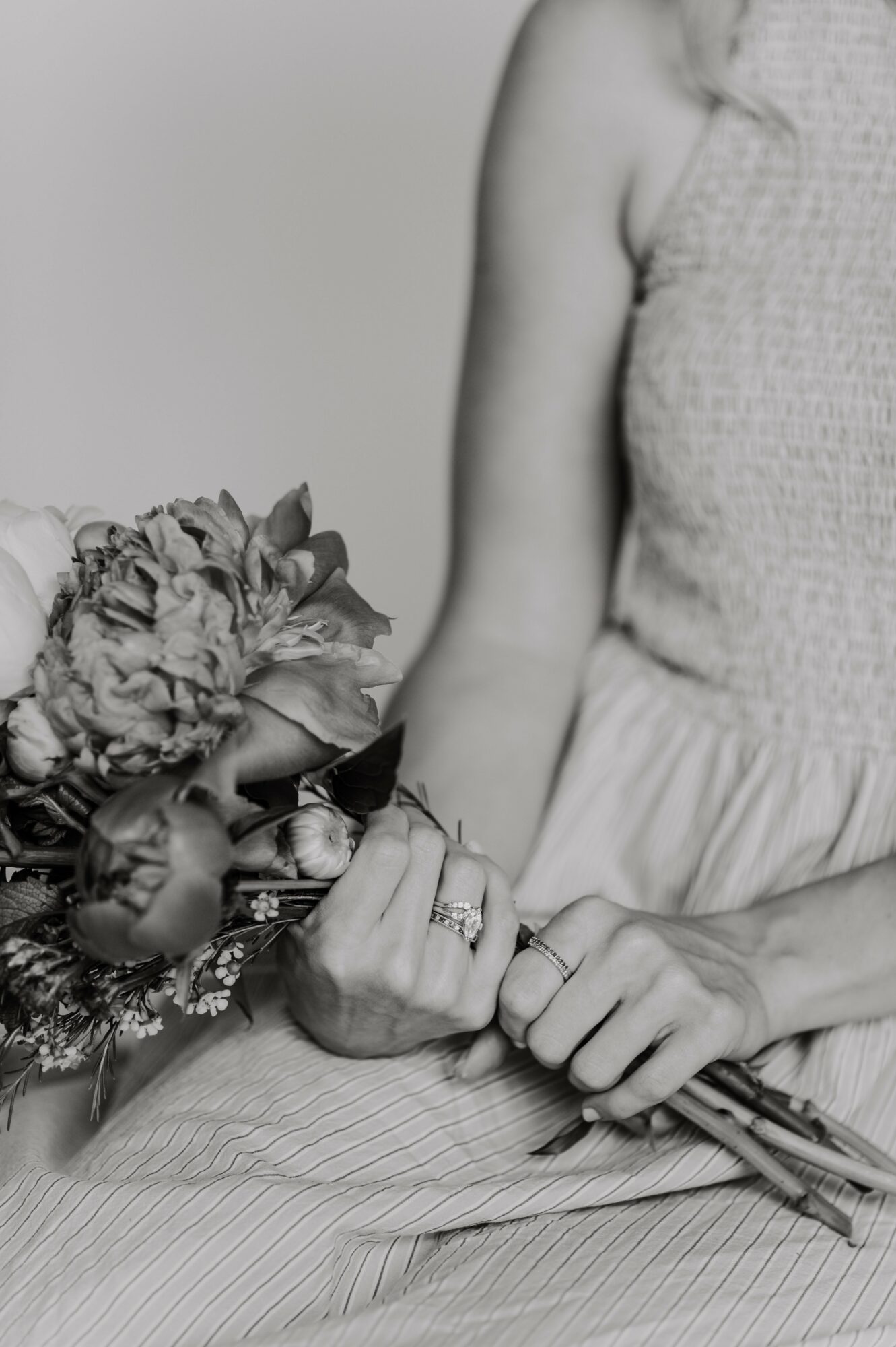 Person holding a bouquet of flowers, wearing a sleeveless top and skirt, with hands resting on lap, rings visible.