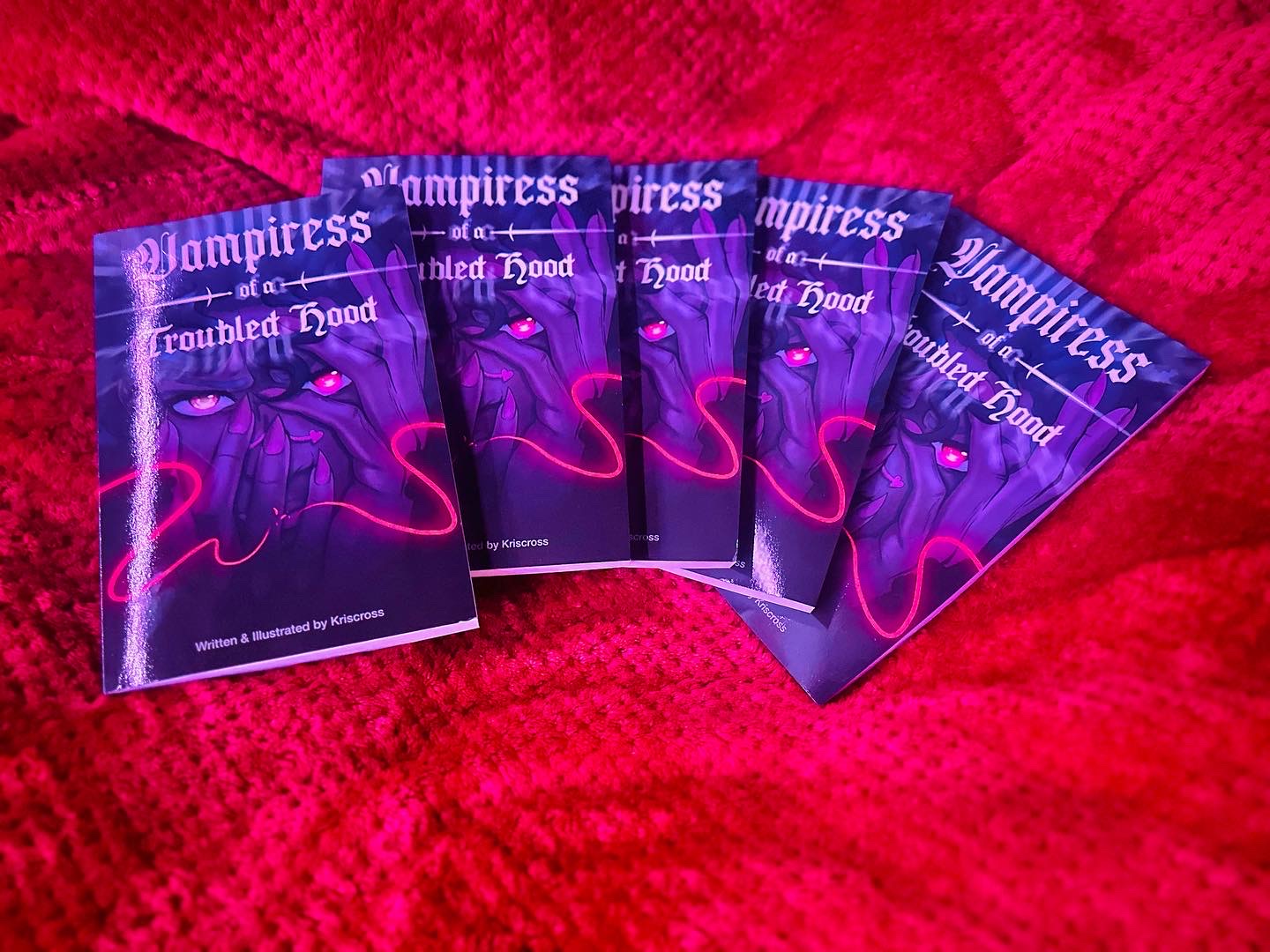 Five copies of a book titled 'Vampire' with a purple cover and pink flamingo illustration, arranged on a red textured surface.