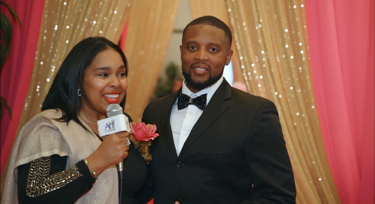 Woman holding microphone and pink rose, man in tuxedo, colorful curtain backdrop, festive event