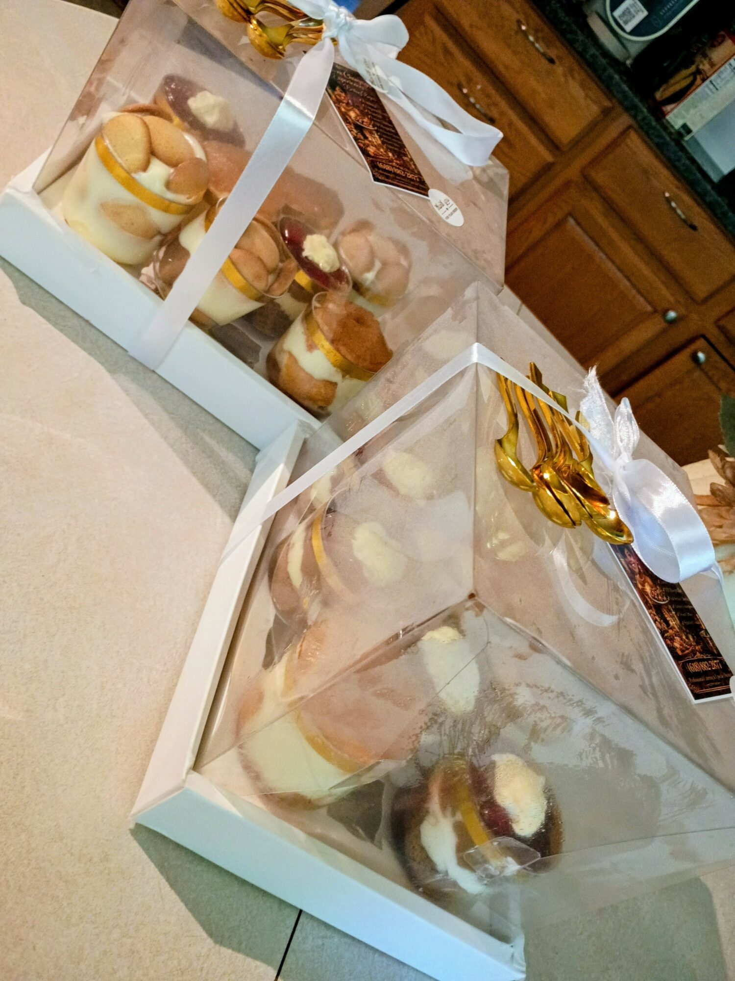Two transparent boxes with cupcakes on a table, with a kitchen in the background.