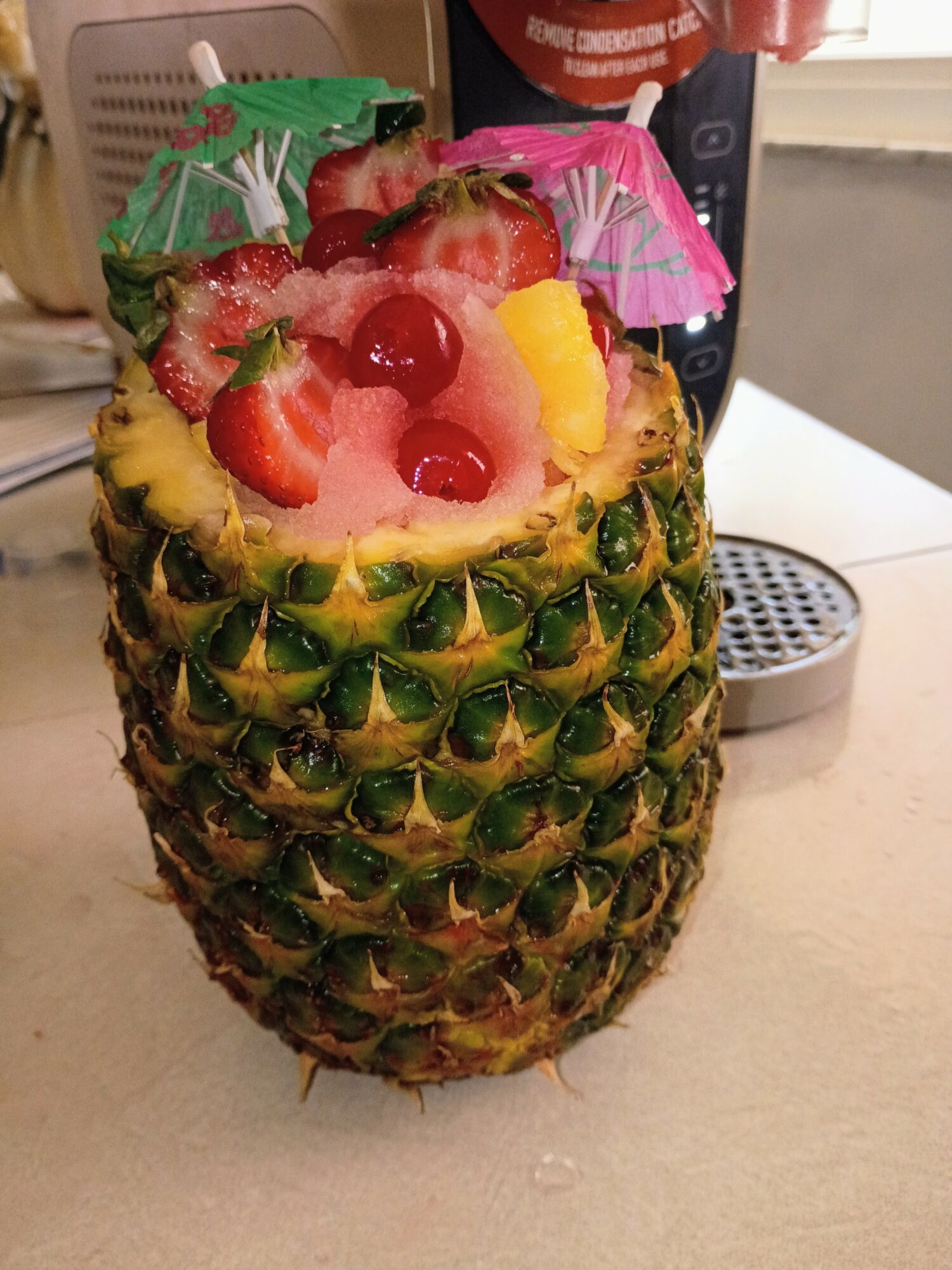 Pineapple with fruit and decorative umbrellas inside, placed on a table.