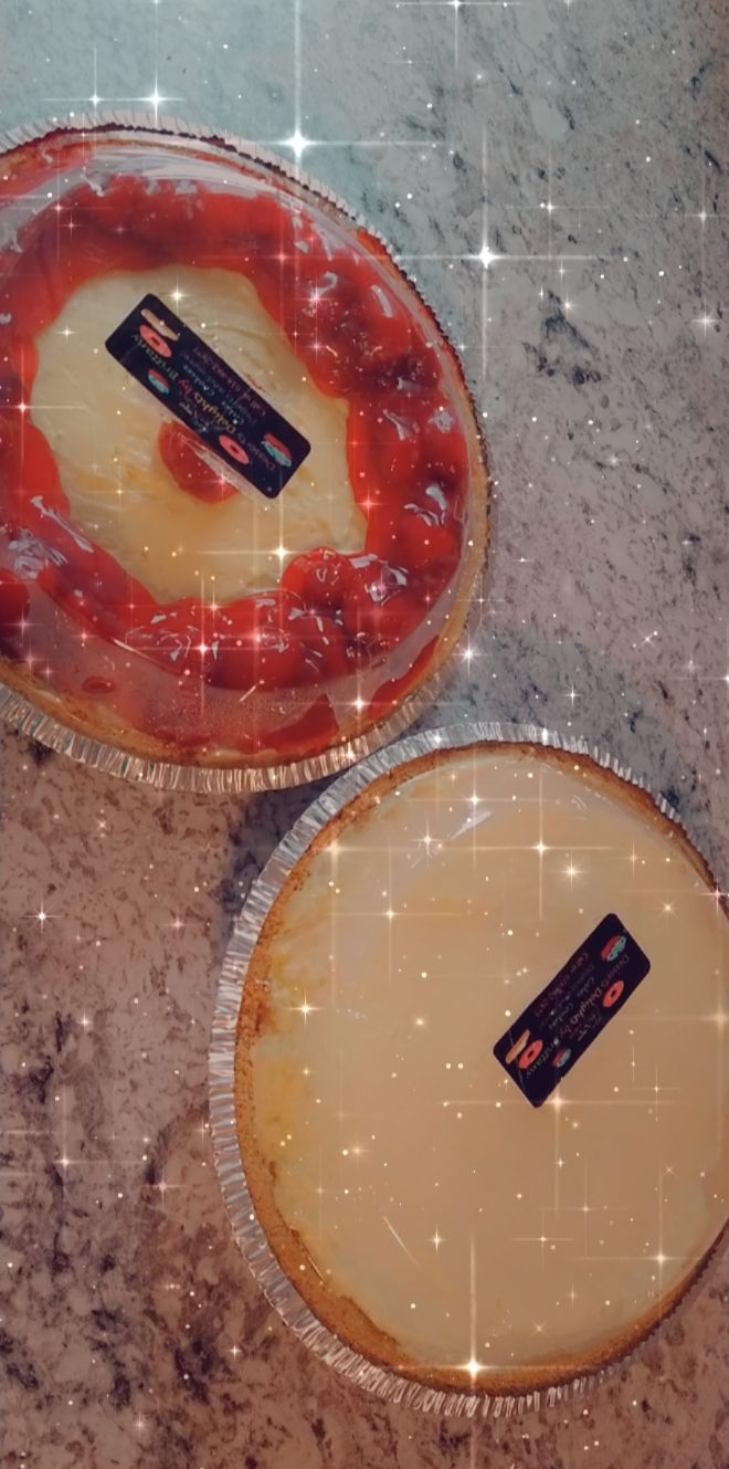 Two round cheesecakes with labels on top, one with a red topping and the other plain, on a gray surface.