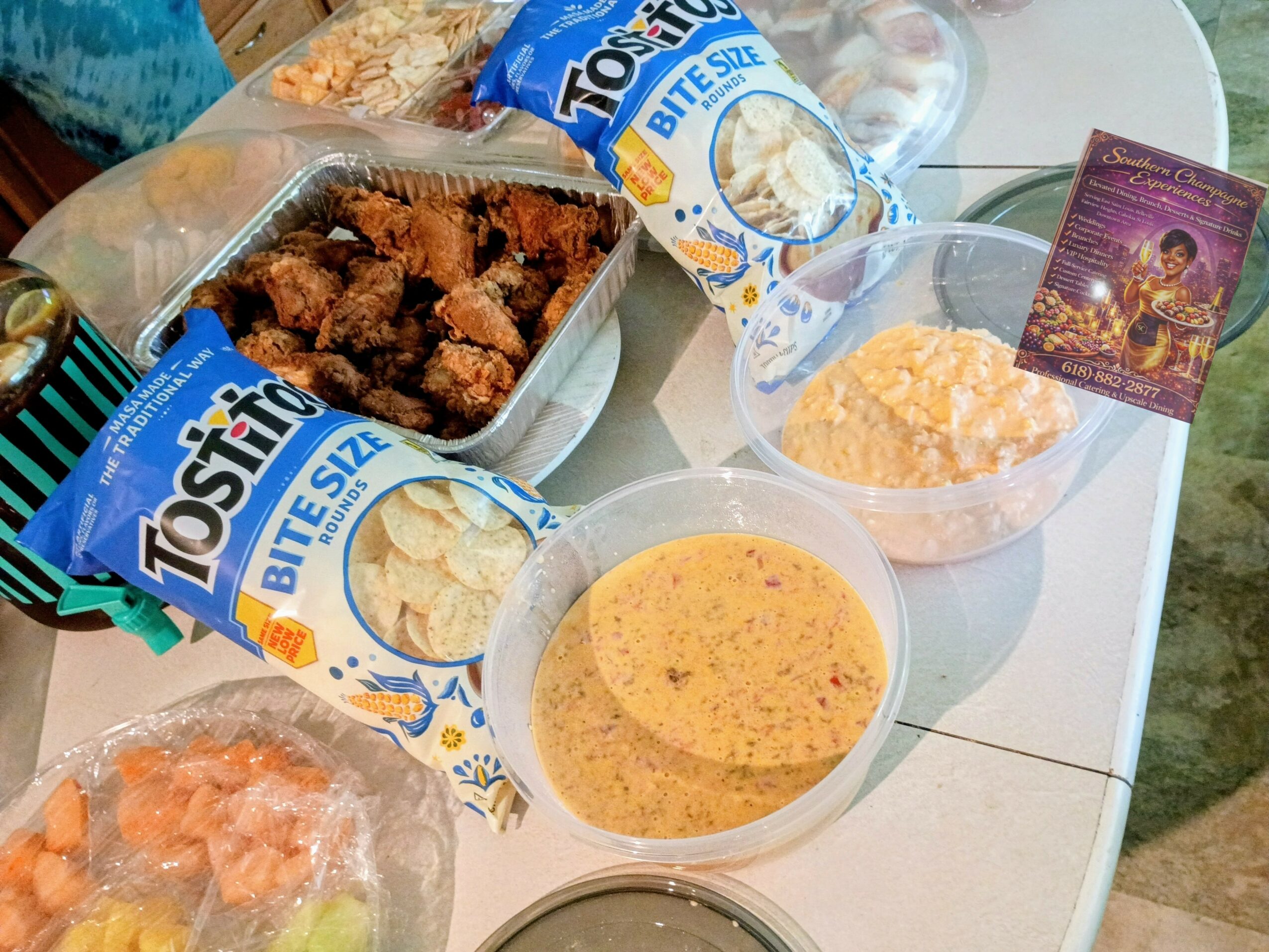 Fried chicken pieces, two bowls of dipping sauces, and snack packs on a table, with a card and a plastic bag in the background.