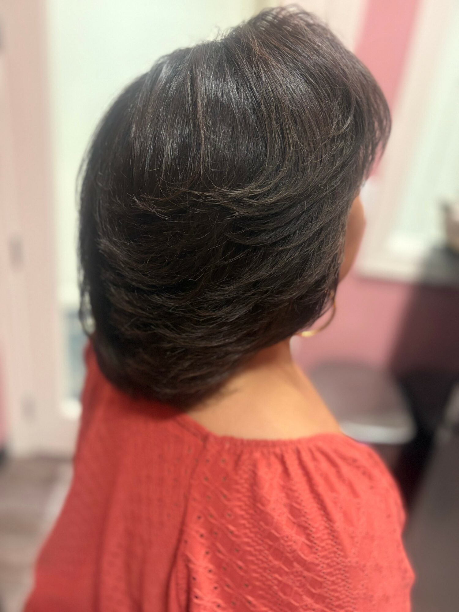 Side view of a woman with short, dark, layered hair wearing a red top in a room.
