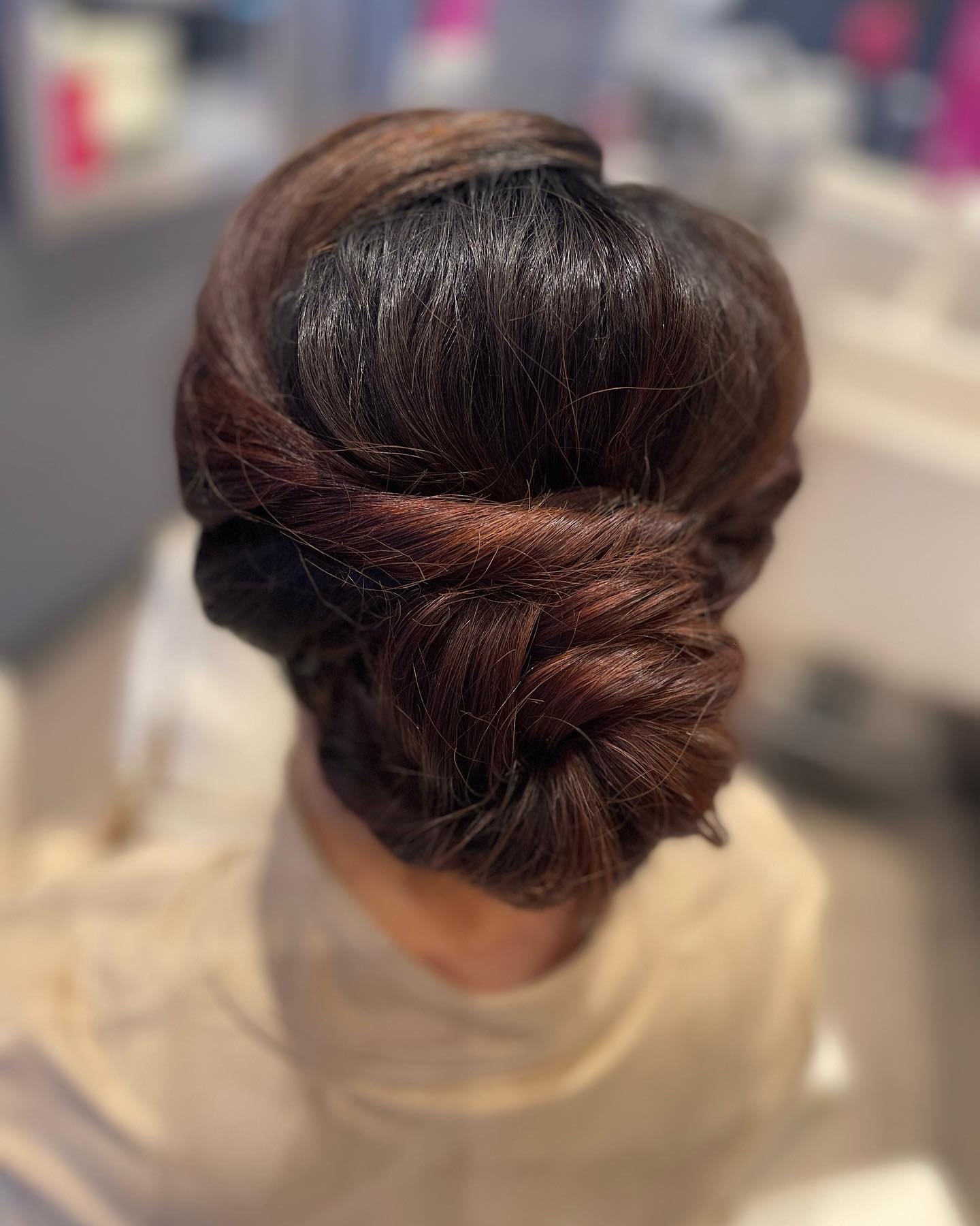 Back view of a woman's styled updo with brown hair, twisted and pinned neatly, in a salon setting.