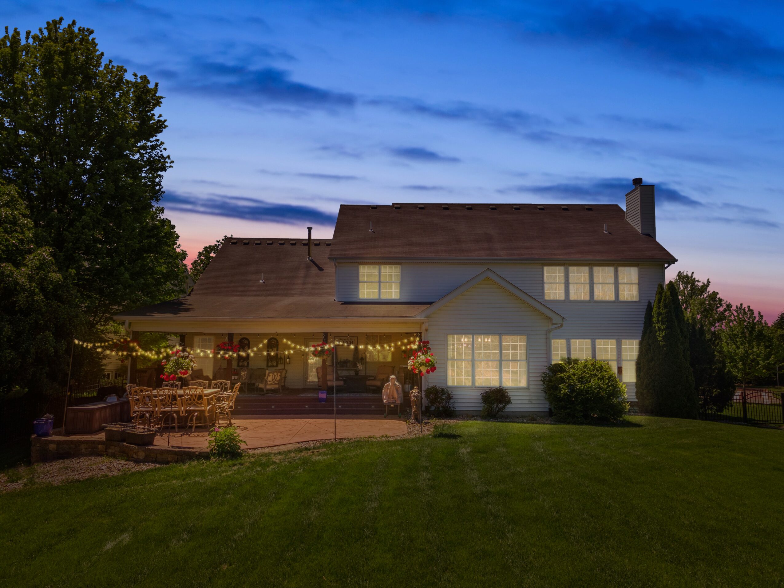 House with a patio, string lights, and a lawn under a blue sky at dusk.