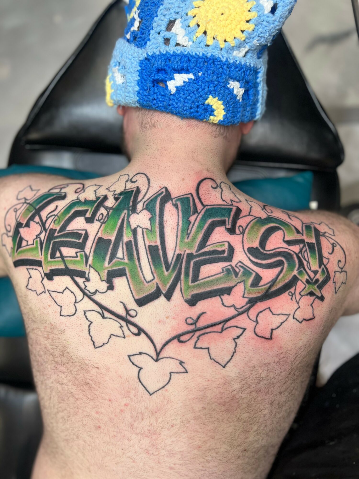 Back of a person with a large tattoo reading 'LEAVES' surrounded by vine and leaf designs.
