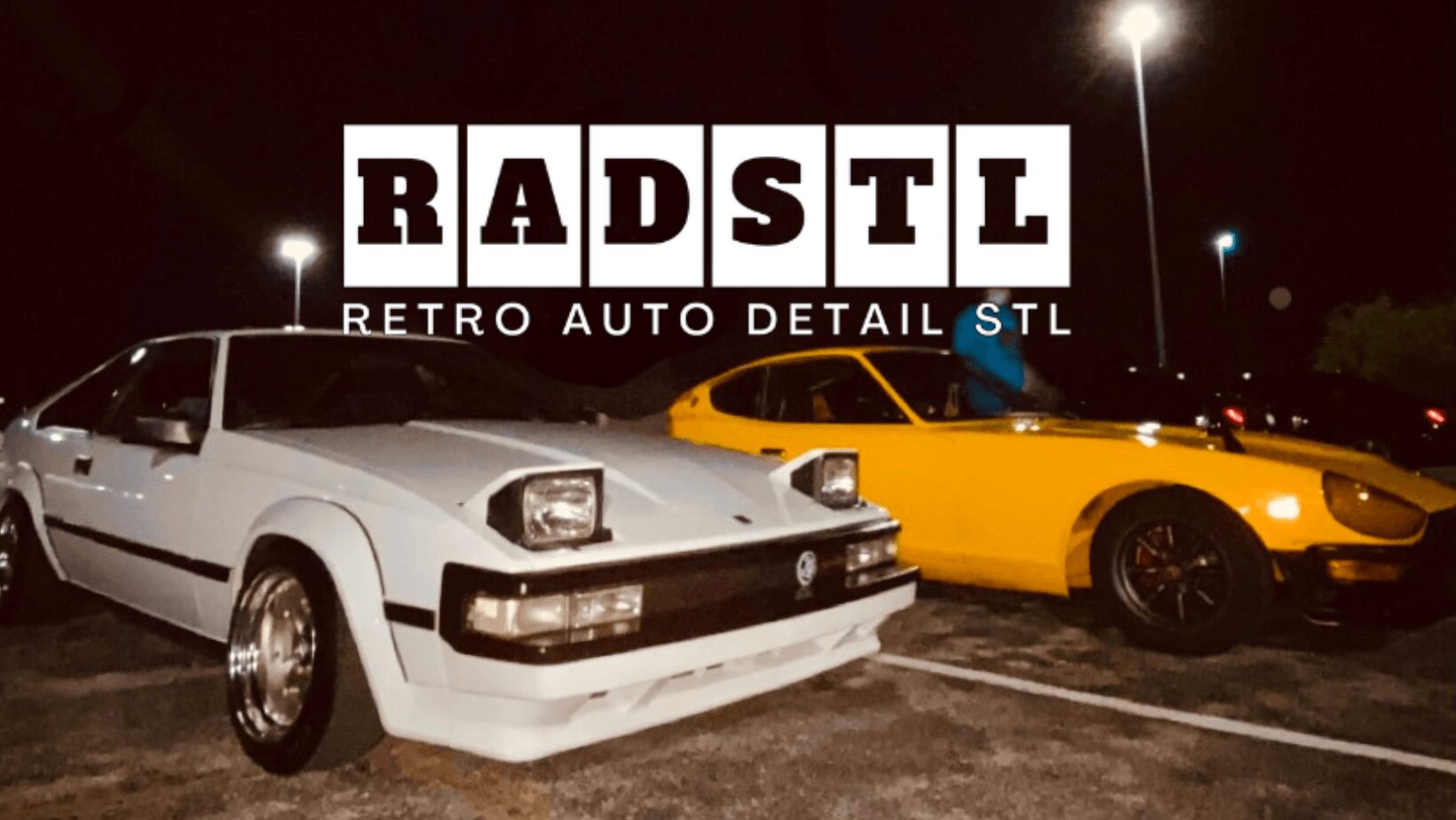 Two classic cars parked side by side at night, one white and one yellow, with a sign reading 'RADSTL' above them.