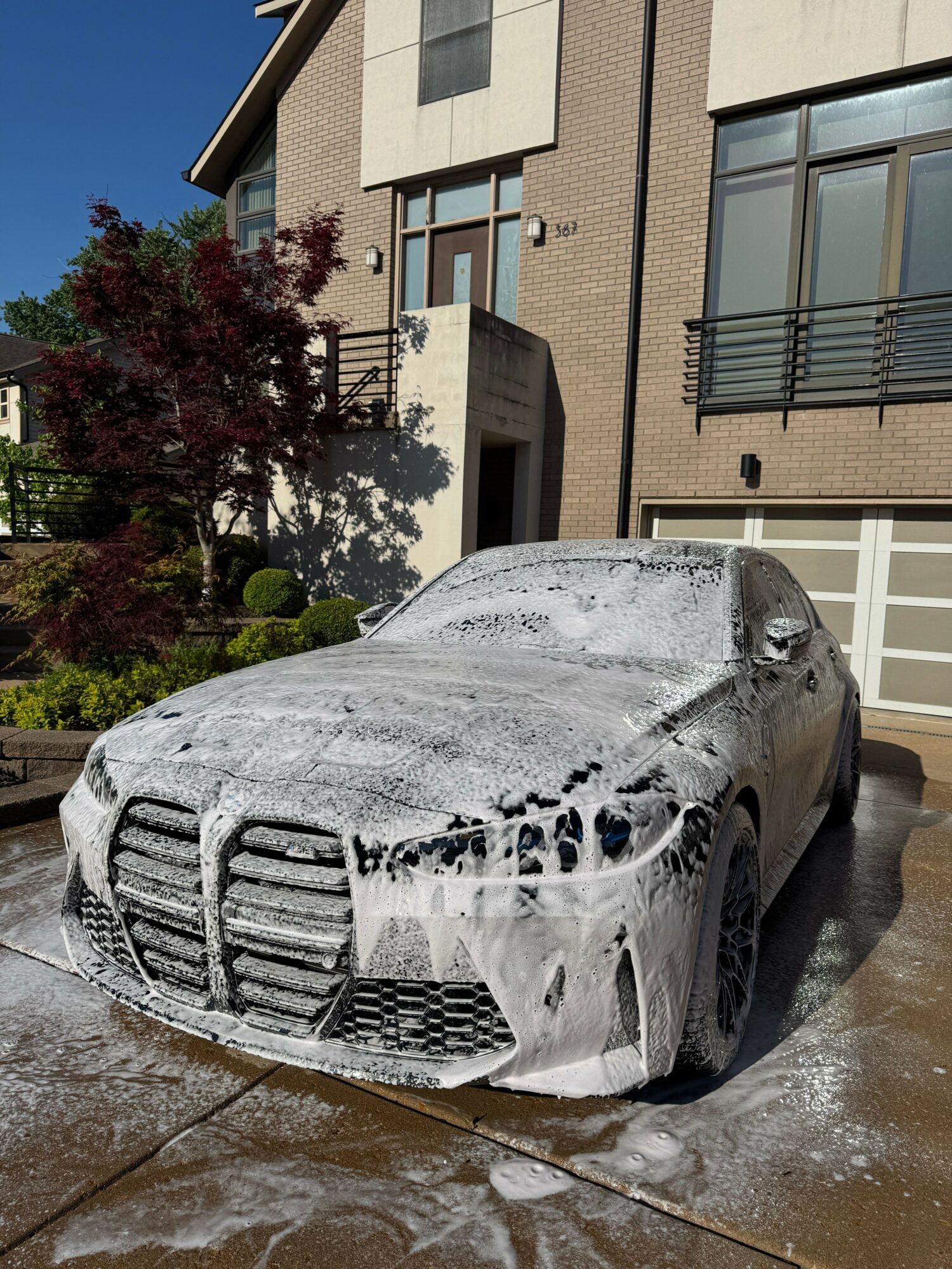 Car covered in snow parked on driveway with house and trees in background.