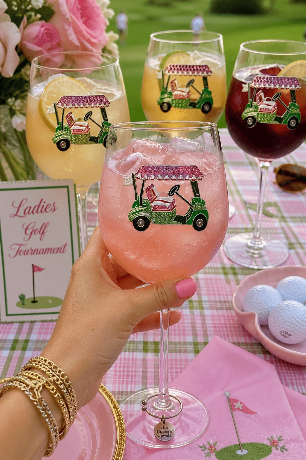 Four glasses with colorful drinks and golf cart decorations on a pink checkered tablecloth, with a sign reading 'Ladies Golf Tournament'.