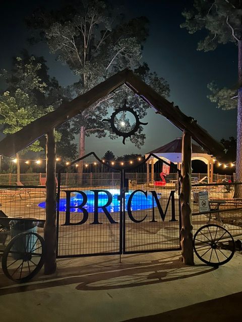Night scene with a metal gate, trees, and a lit area in the background, with a bicycle wheel visible. Word 'BRICK' on gate.