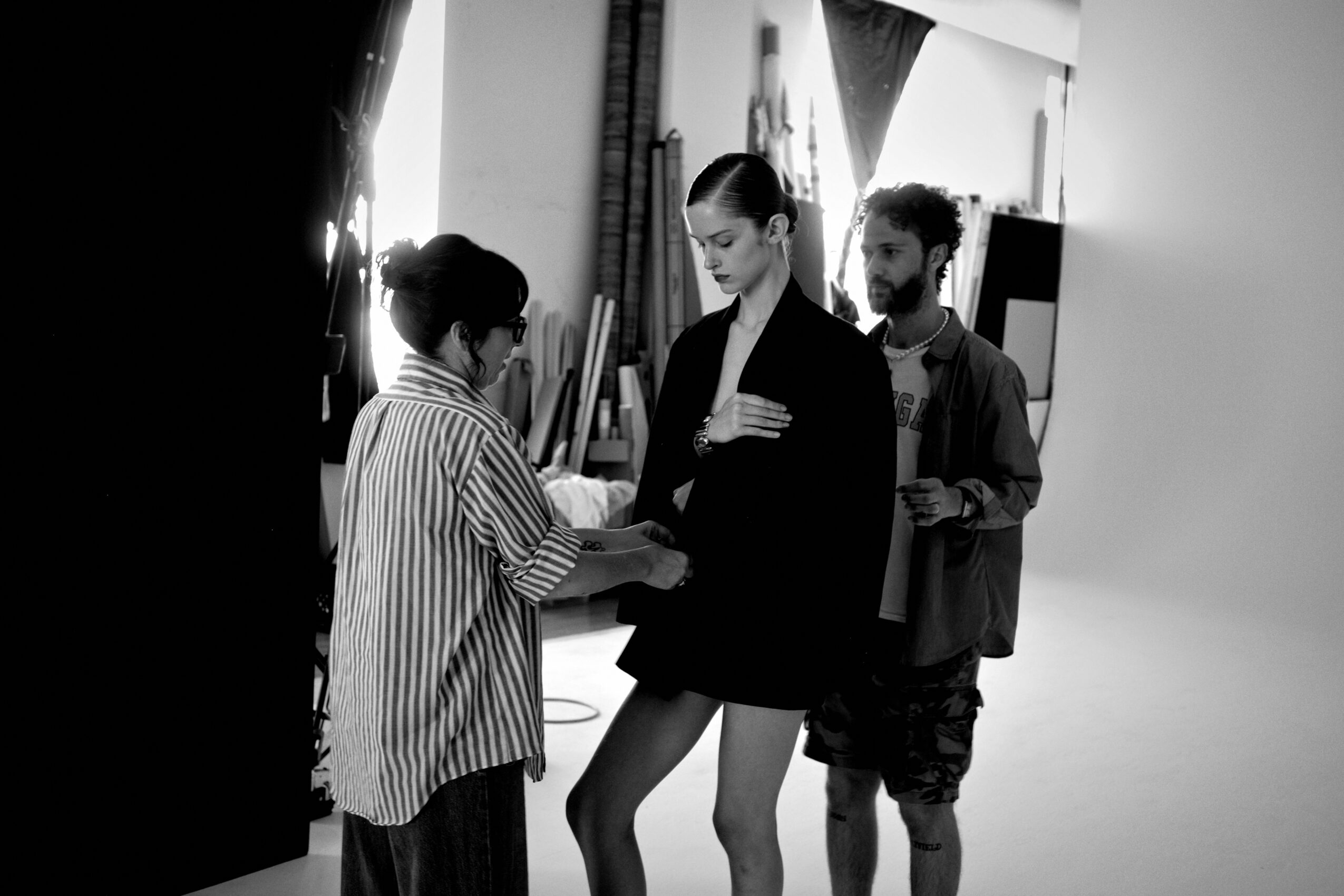 Three people engaged in conversation indoors, one woman and two men, with a bright background and studio setting.