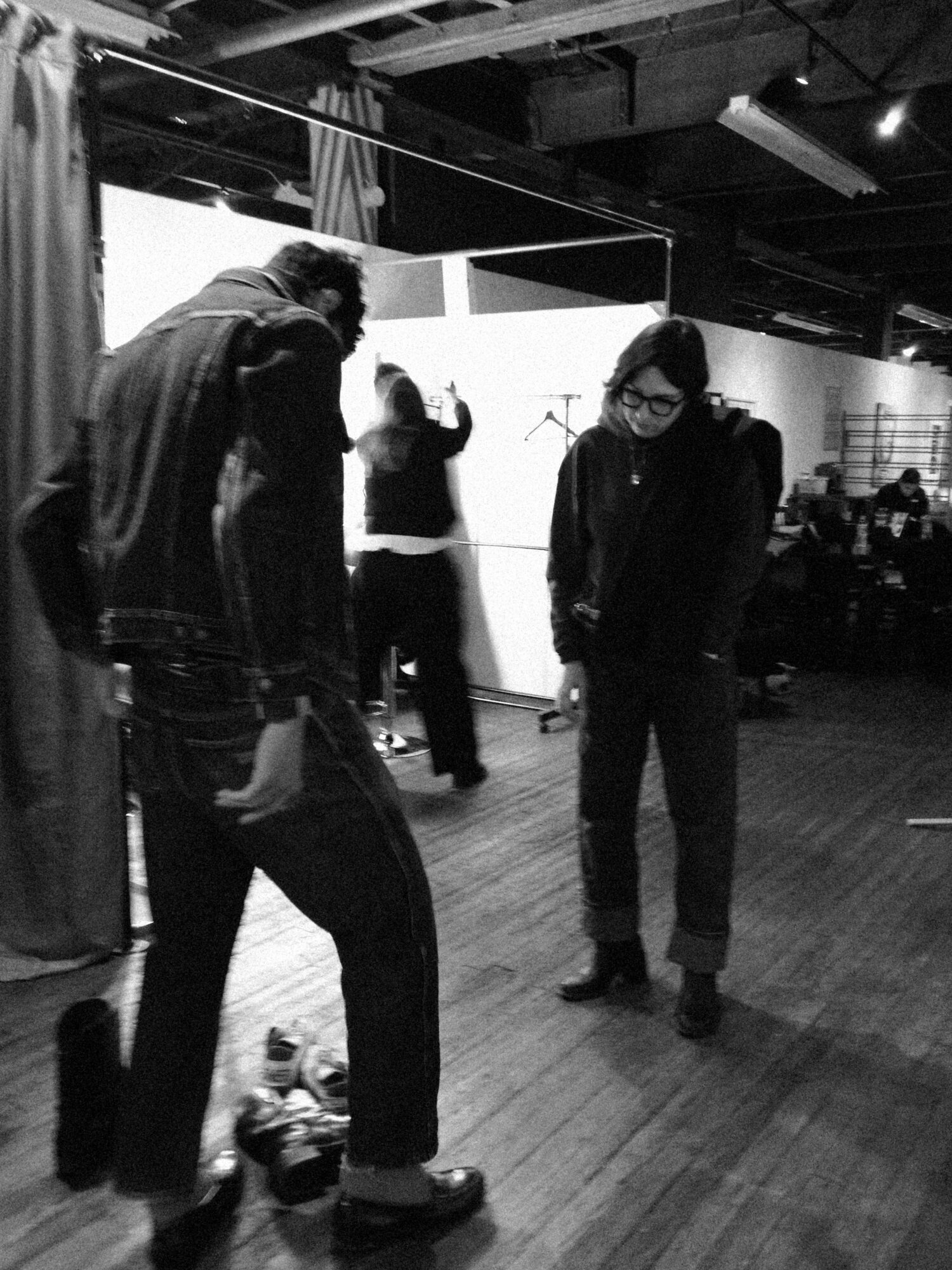 Three people standing in a room with wooden flooring, one person holding a bag, and a person in the background.
