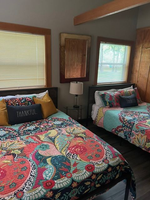 Bedroom with bed, colorful quilt, pillows, window, and wooden furniture, viewed from the side.