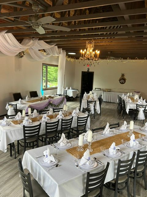 Dining room with tables set for a formal event, decorated with white tablecloths, napkins, and chairs, and a chandelier in the background.