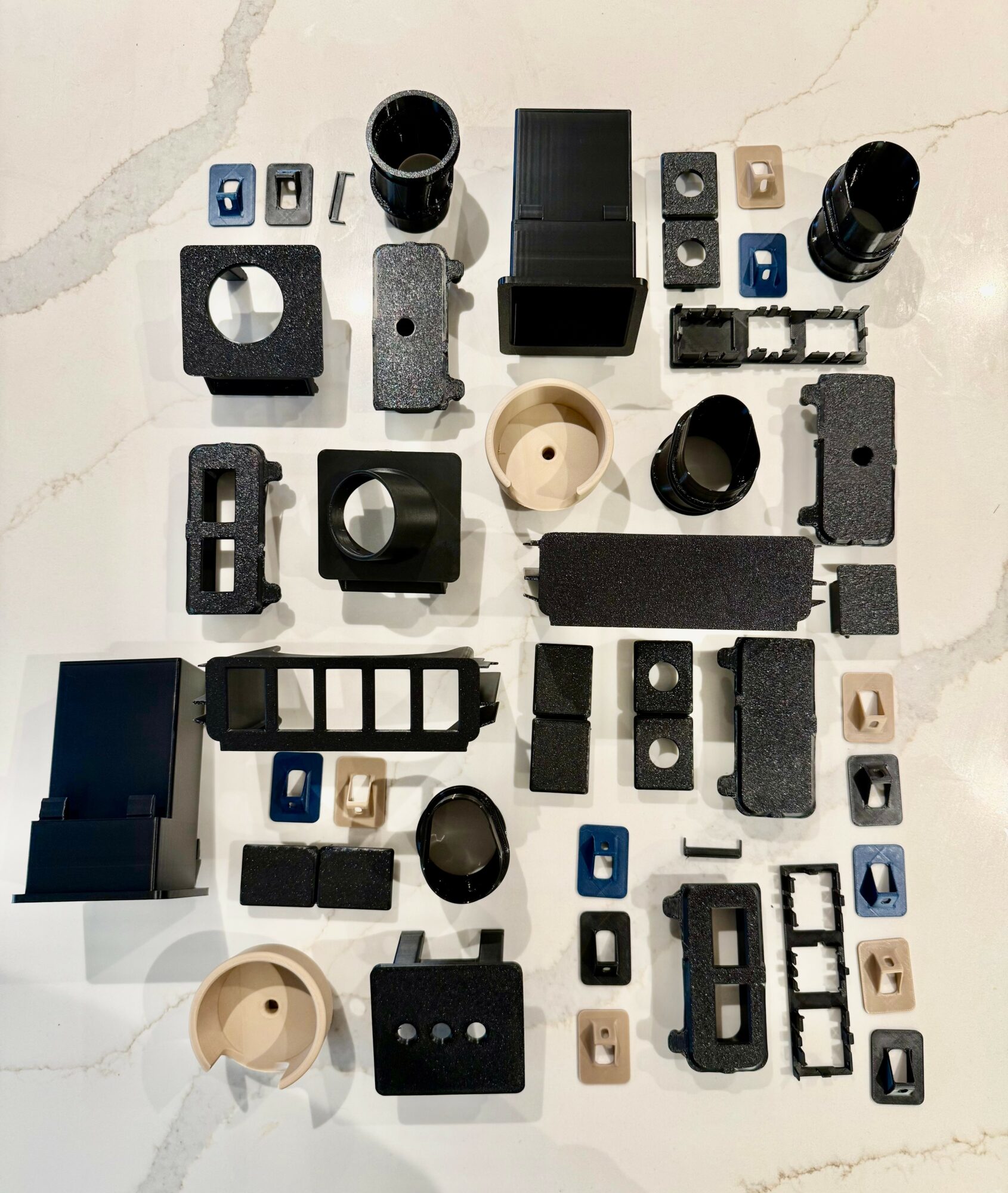 Various black, gray, and beige mechanical parts and components arranged on a white surface.