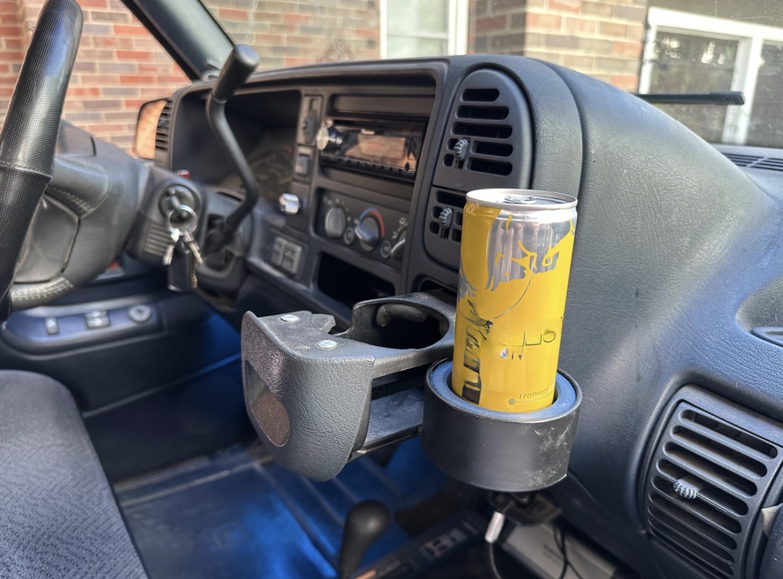 Dashboard of a vehicle with a yellow can in a cup holder, and various controls visible.