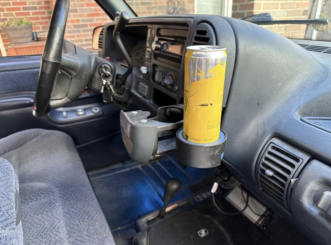 Dashboard of a vehicle with a yellow beverage can holder attached to the right side, containing a yellow can.