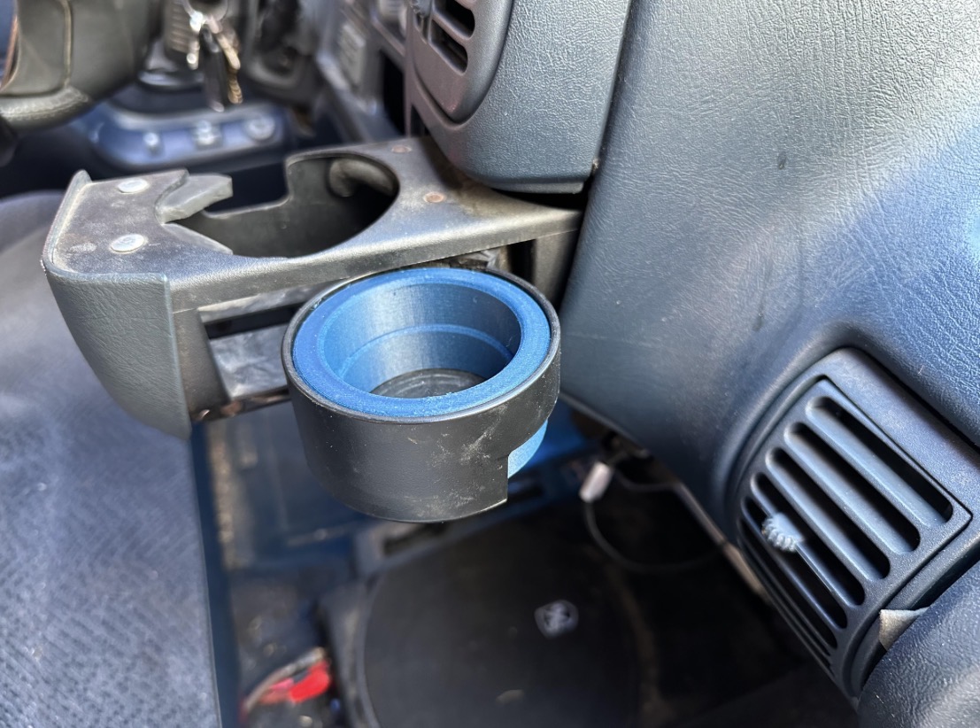 Car interior with a blue and black cup holder attached to the dashboard, near the air vent.