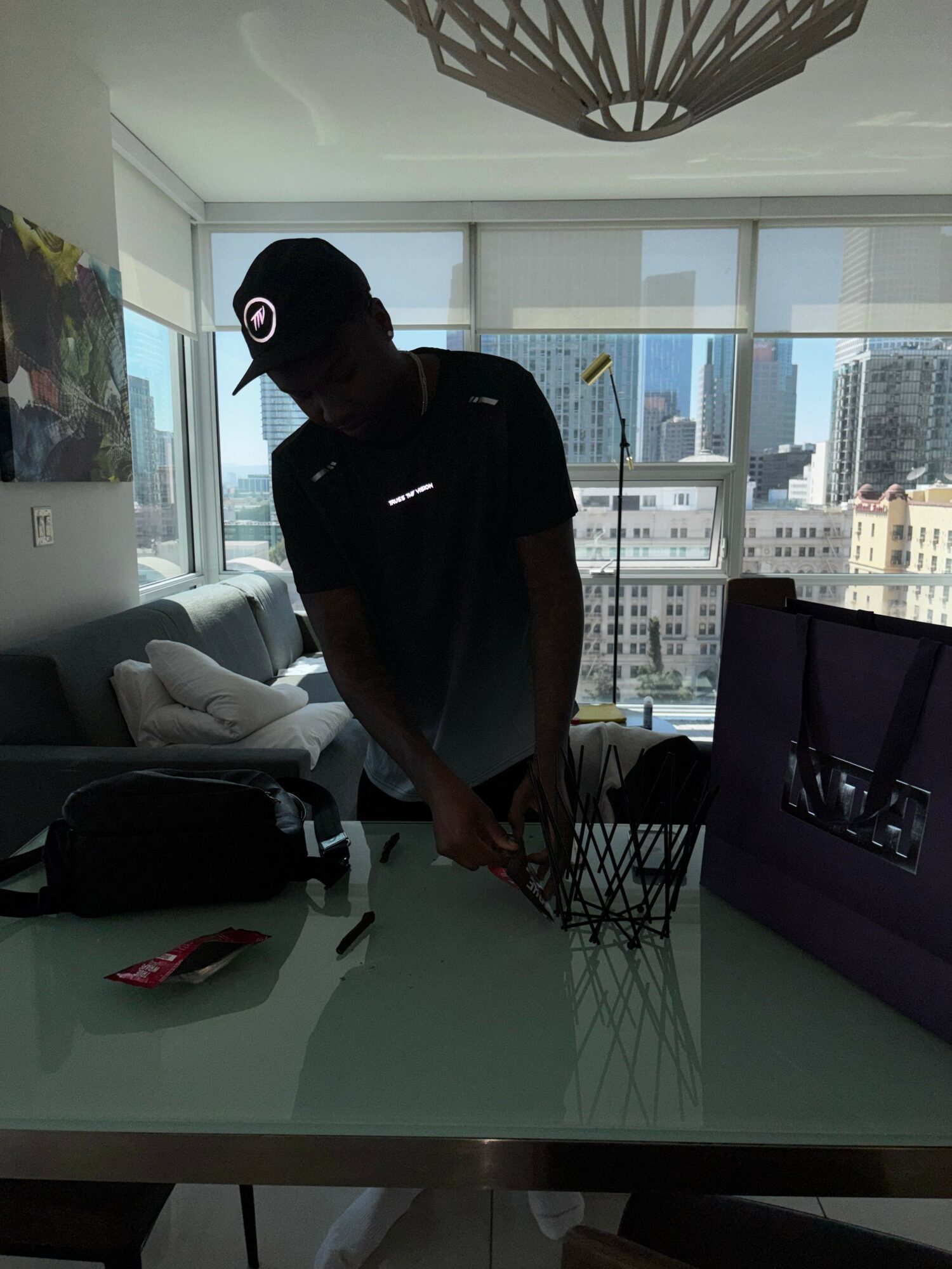 Person standing in a modern office with large windows, cityscape view, and a glass table with items on it.