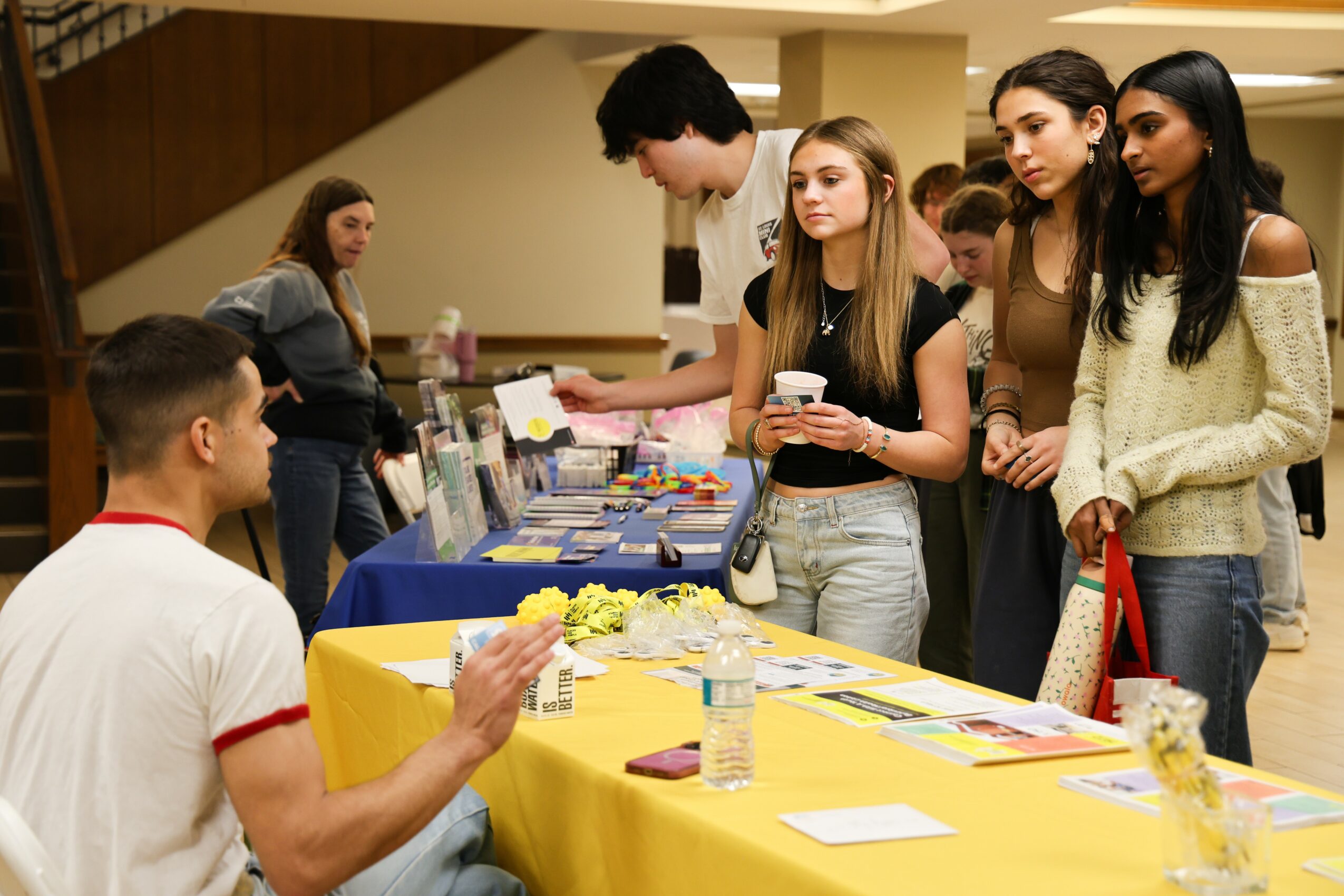 Group of young people at a table with various items, engaging in conversation indoors.