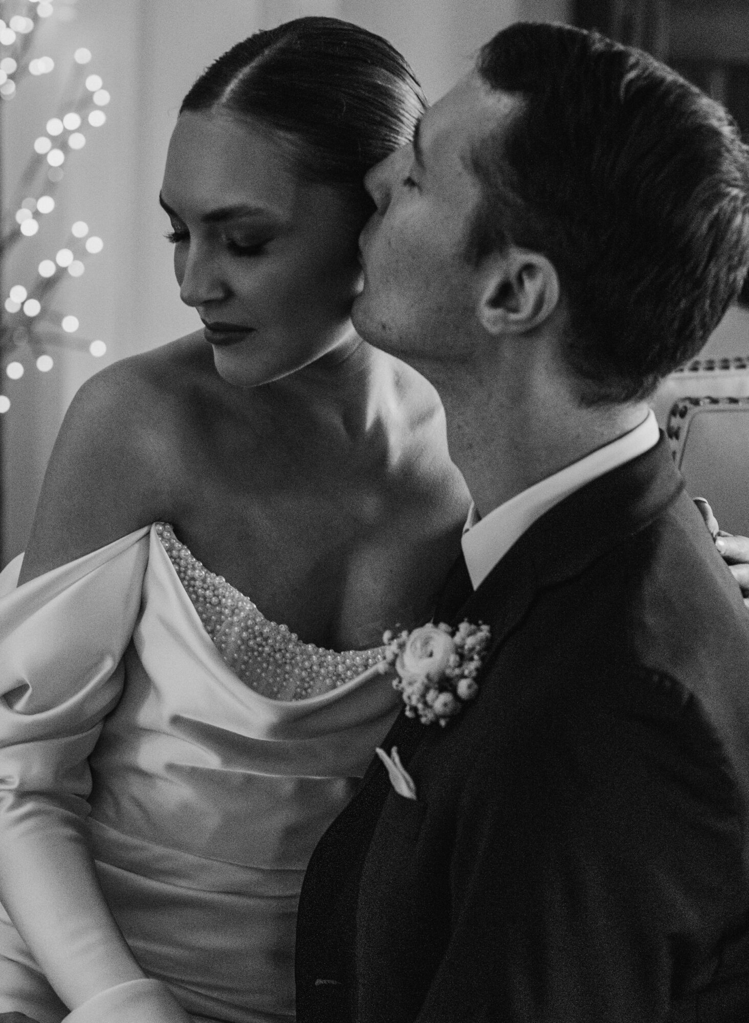A couple in wedding attire sharing a kiss, with the woman in a strapless dress and the man in a suit, in black and white.