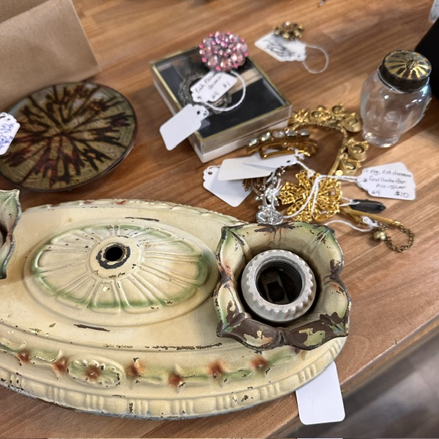 Decorative ceramic tray with a circular opening, surrounded by jewelry, a glass jar, and a book on a wooden surface.