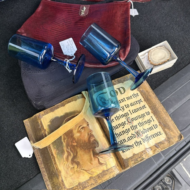 Three blue wine glasses, a box with a round object, a red bag, and a book with a portrait of Jesus on a surface.