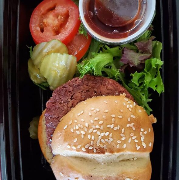 Hamburger with sesame seed bun, lettuce, tomato, pickles, and a side of salad with dressing.