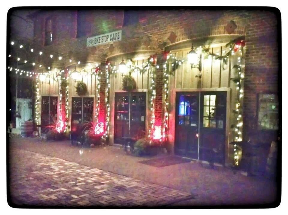 Building exterior decorated with string lights and potted plants, illuminated at night, with cobblestone street in foreground.