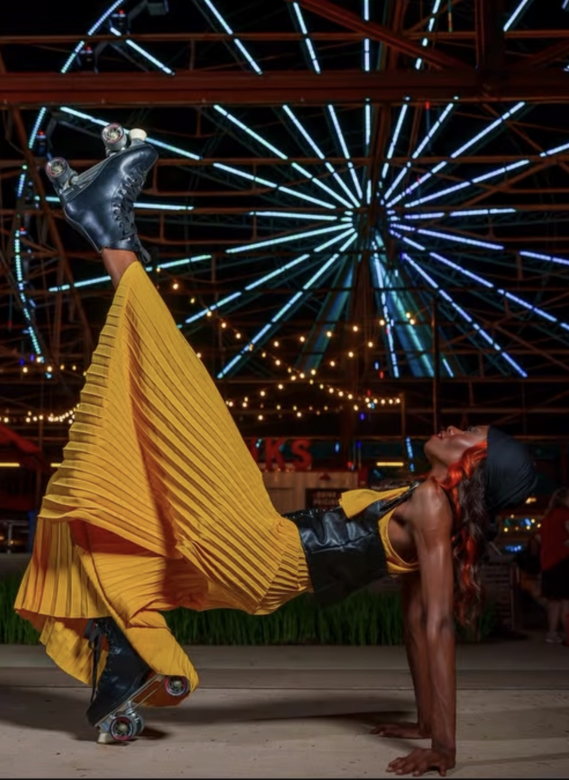 Performer in a yellow dress and roller skates poses with a dog at a carnival with a Ferris wheel in the background.