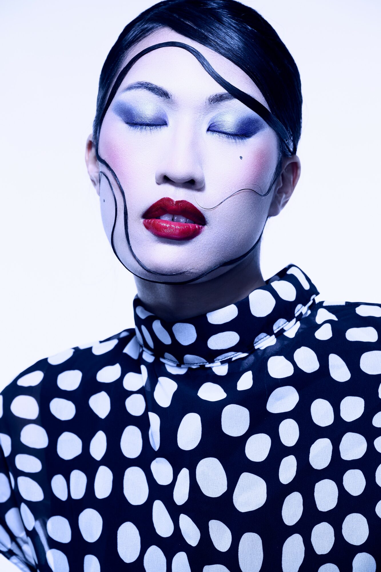 Woman with bold makeup and a black and white polka dot top, with artistic face paint and stylized lines on face.