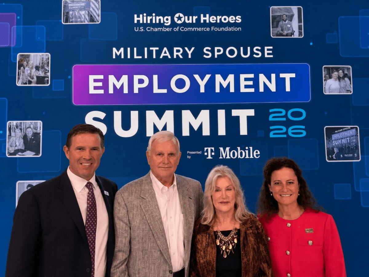Four people standing together at a military spouse employment summit, with a blue background and event text.