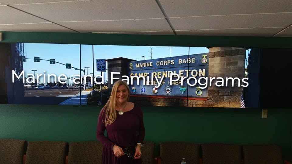Woman standing in front of a large digital display showing Marine Corps Base signage.