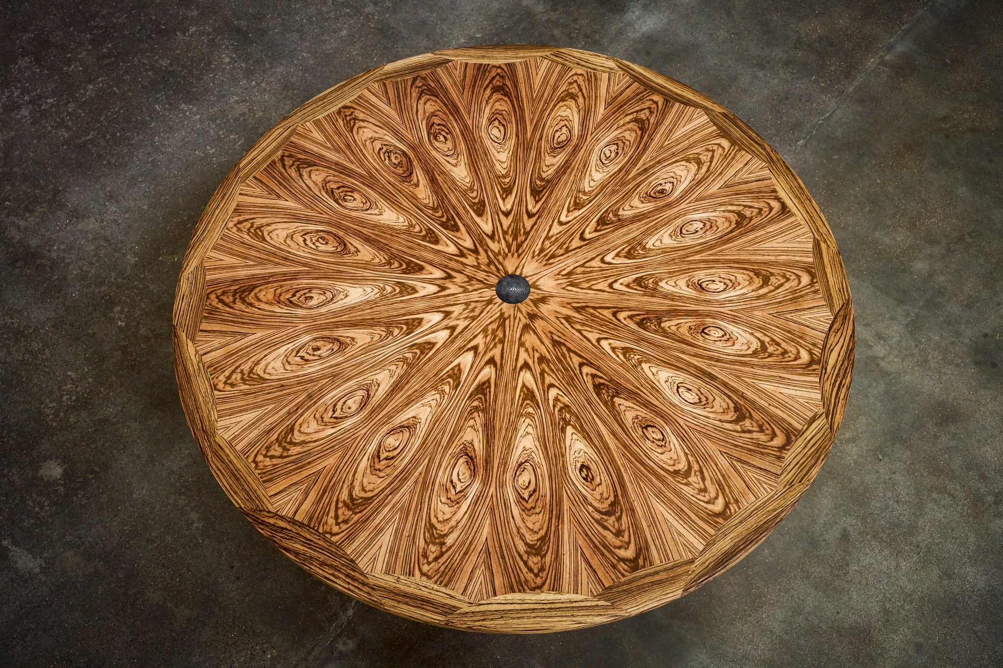 Round wooden table with intricate carved pattern on top, placed on a dark surface.