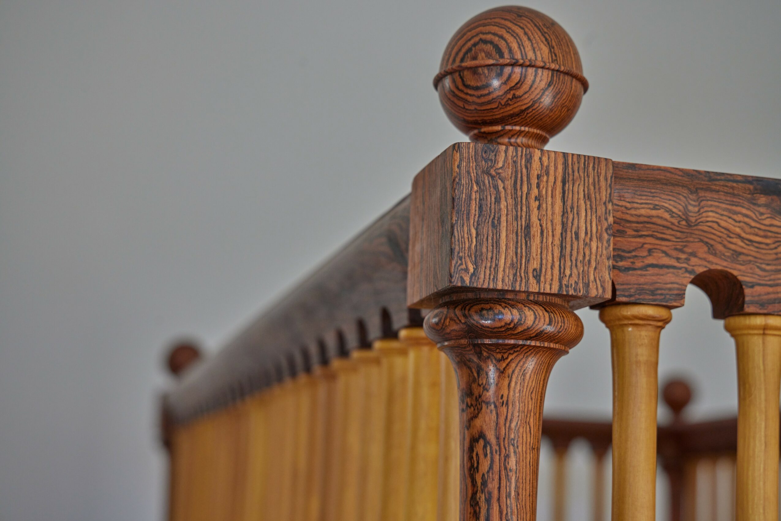 Close-up of a wooden bedpost with detailed grain and rounded top, part of a bed frame with vertical slats.