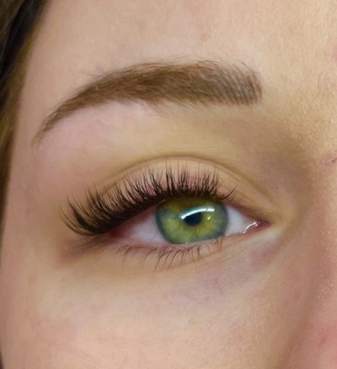 Close-up of a person's eye with green iris, long eyelashes, and well-defined eyebrow.
