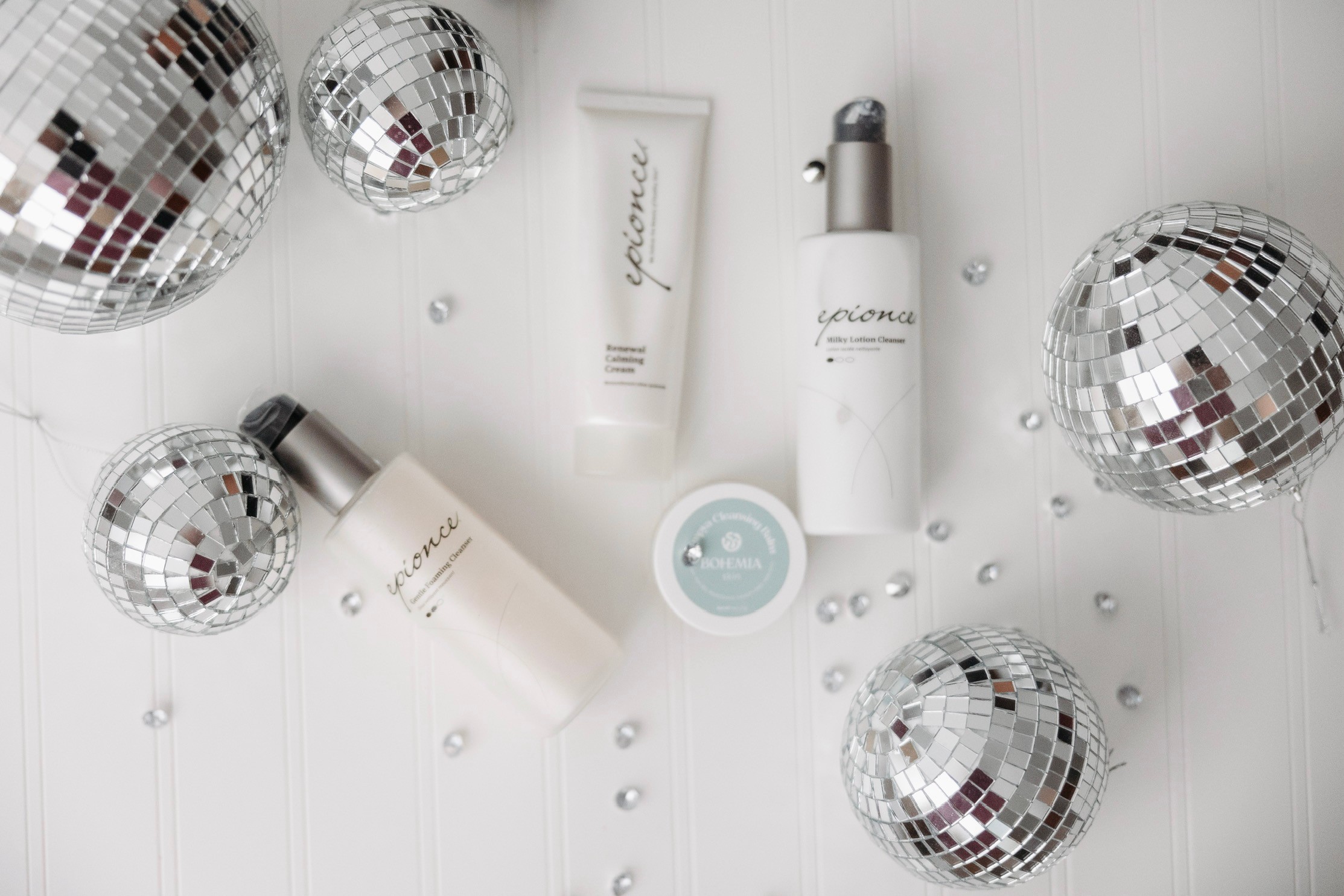 Cosmetic products and disco balls arranged on a white surface, with scattered small white beads or pearls.