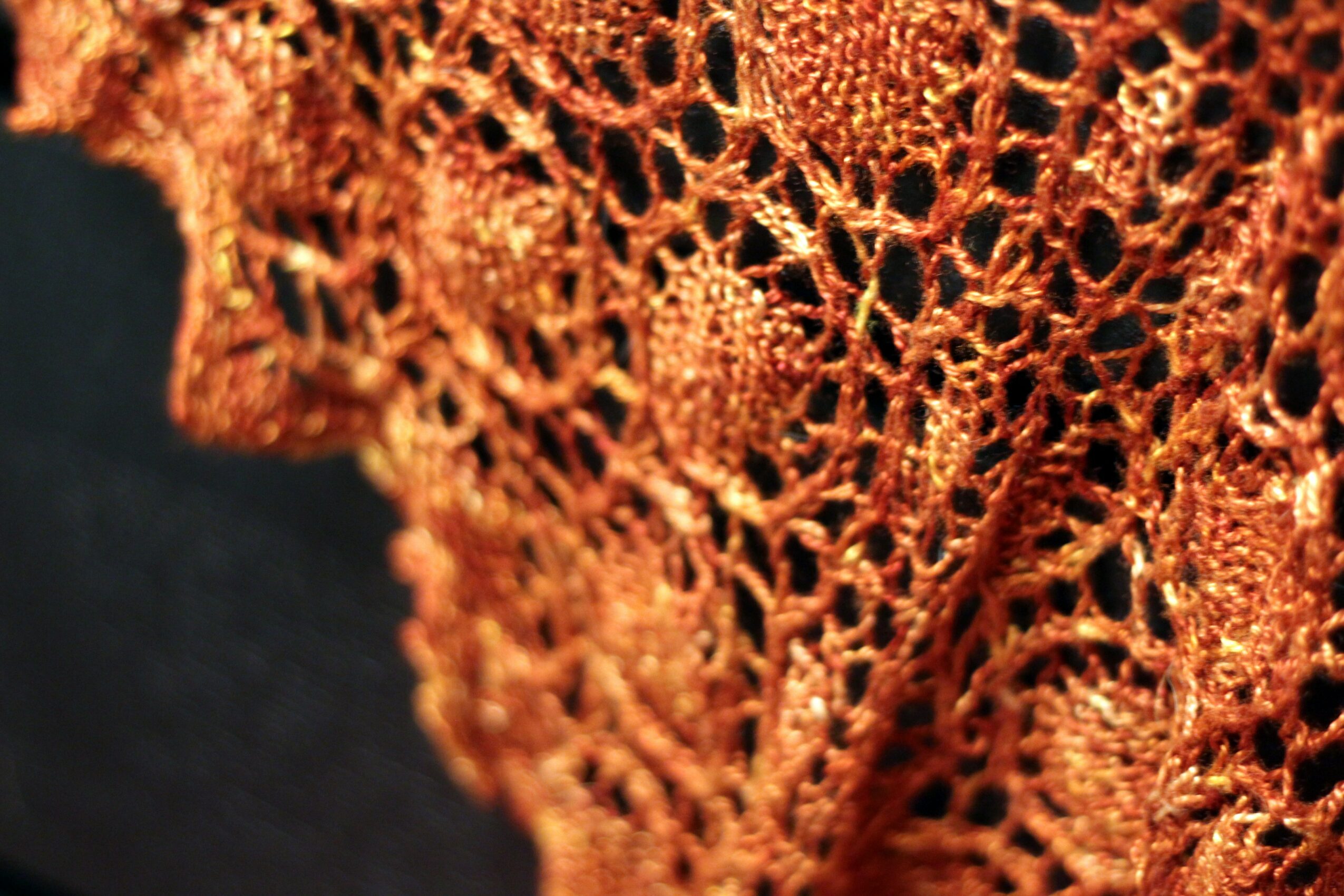 Close-up of orange lace fabric with intricate openwork pattern, against a black background.
