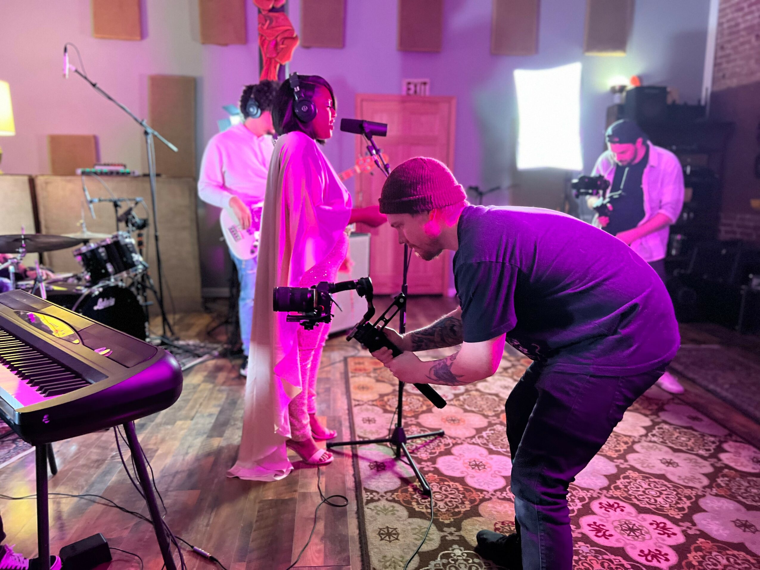 People in a music studio wearing VR headsets, with a person adjusting equipment, and musical instruments visible.
