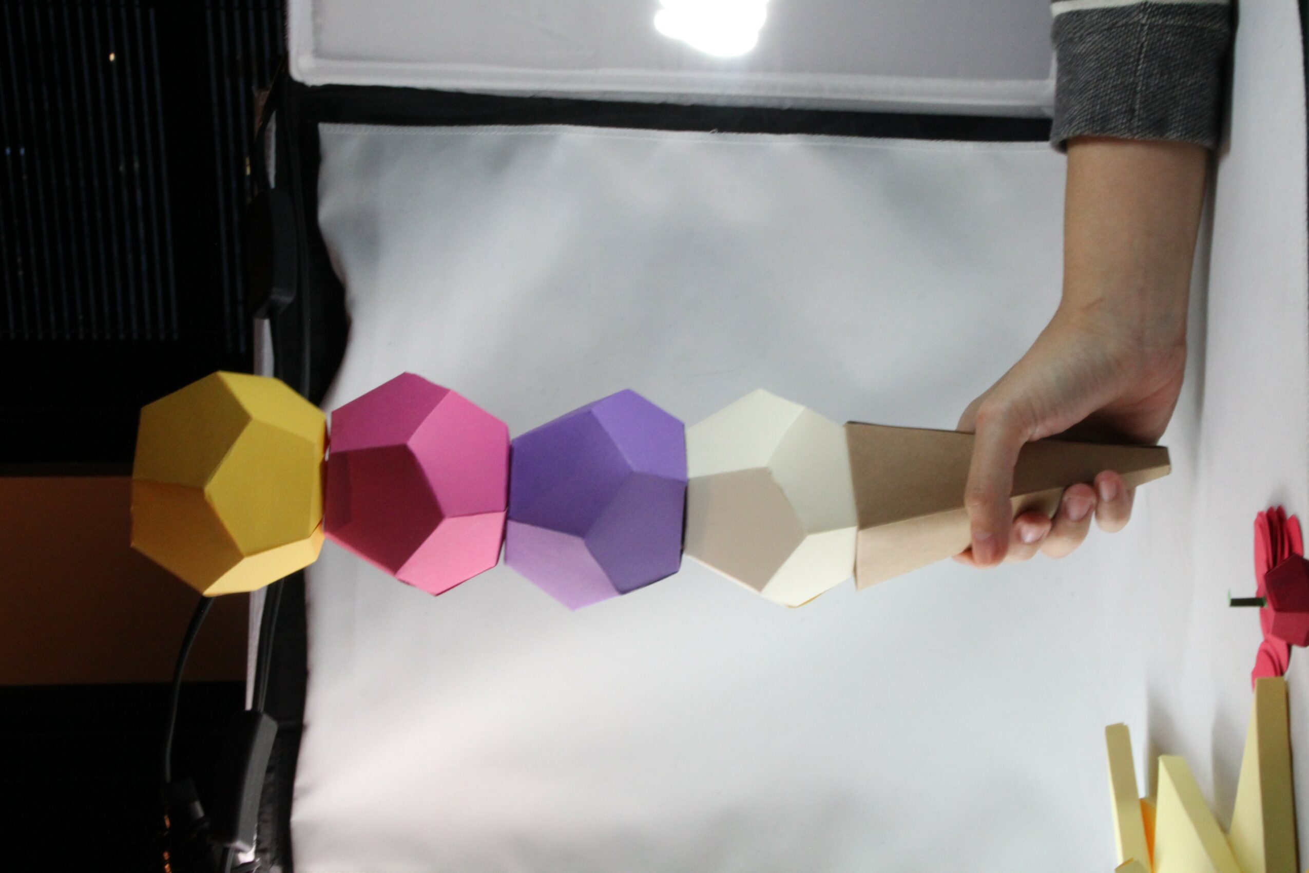 Person holding a wooden stick with colorful geometric shapes stacked on it, on a white background.
