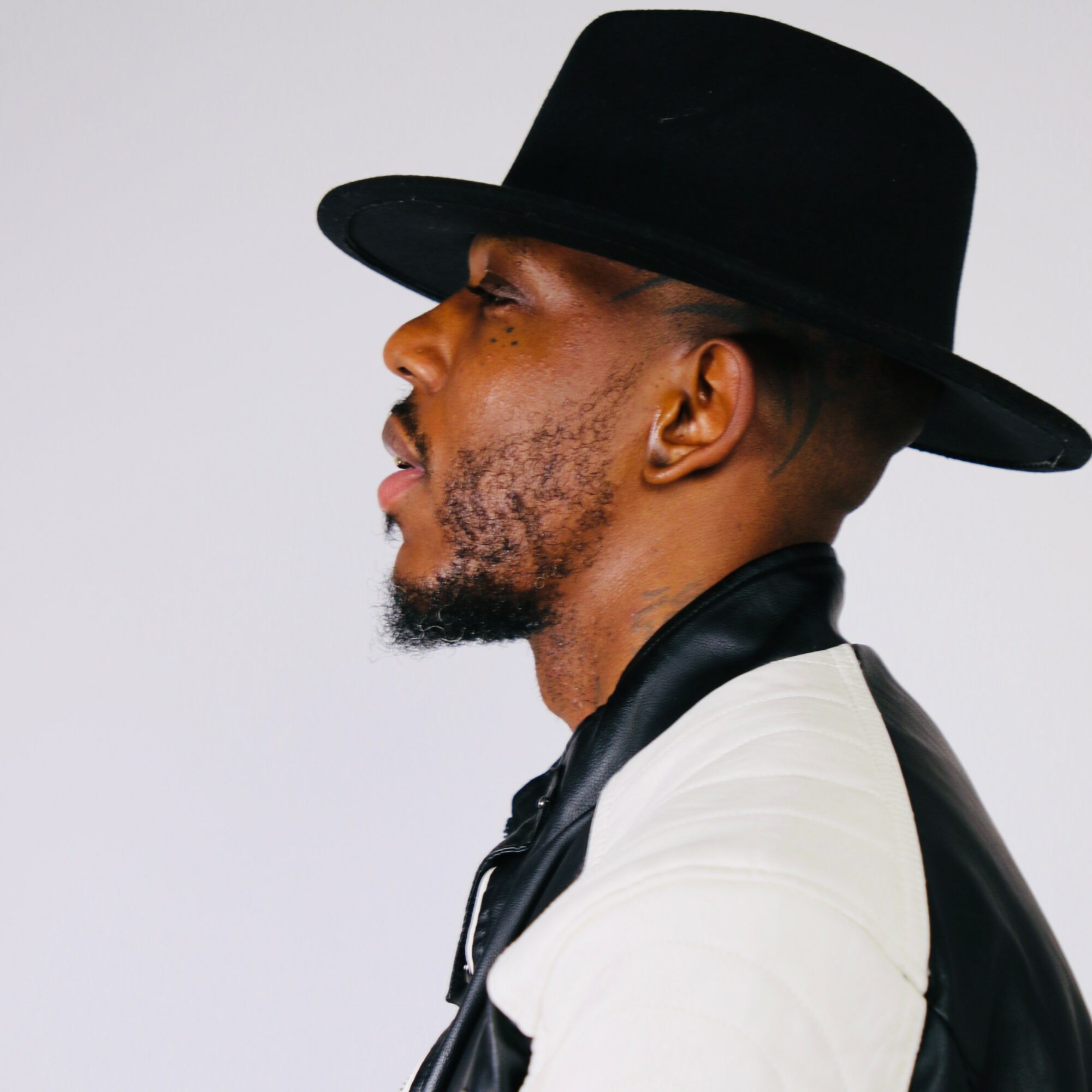 Side profile of a man wearing a black hat and a black and white jacket, facing left.