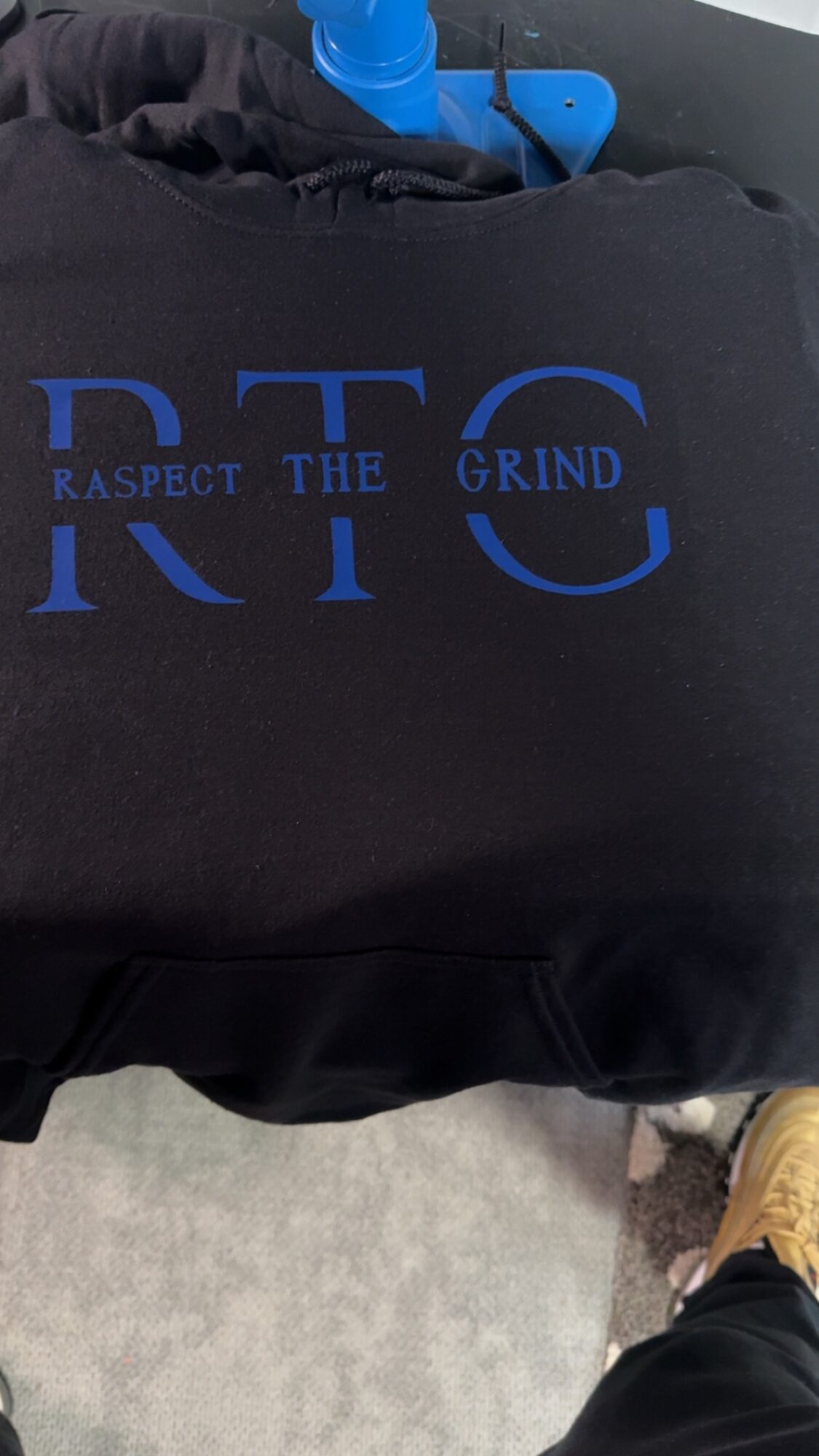 Black fabric with blue text reading 'RESPECT THE GRIND' and large blue letters 'R T G'.